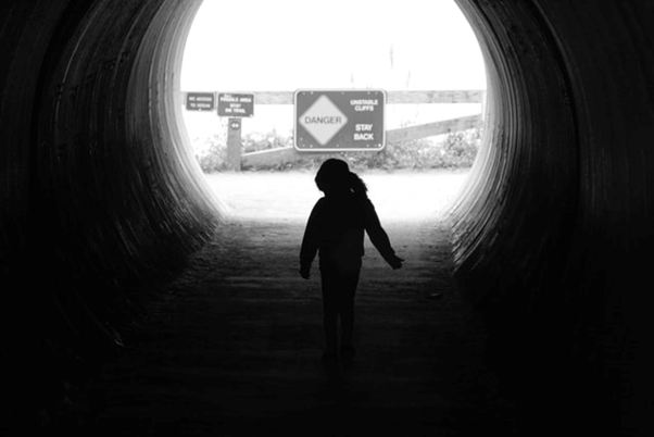 Child walking through dark tunnel toward “Danger” sign at end