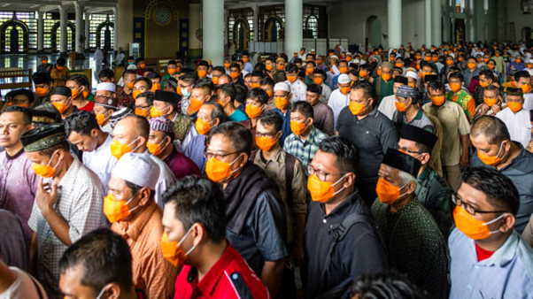 Crowds of people wearing orange face masks attend prayers at a Mosque