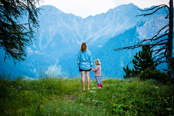 Woman holding hand of child looking at mountains