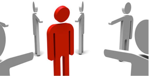 Six grey barely three dimensional person icons standing in a circle who are all pointing to a red barely two dimensional person icon in the middle of the graphic.