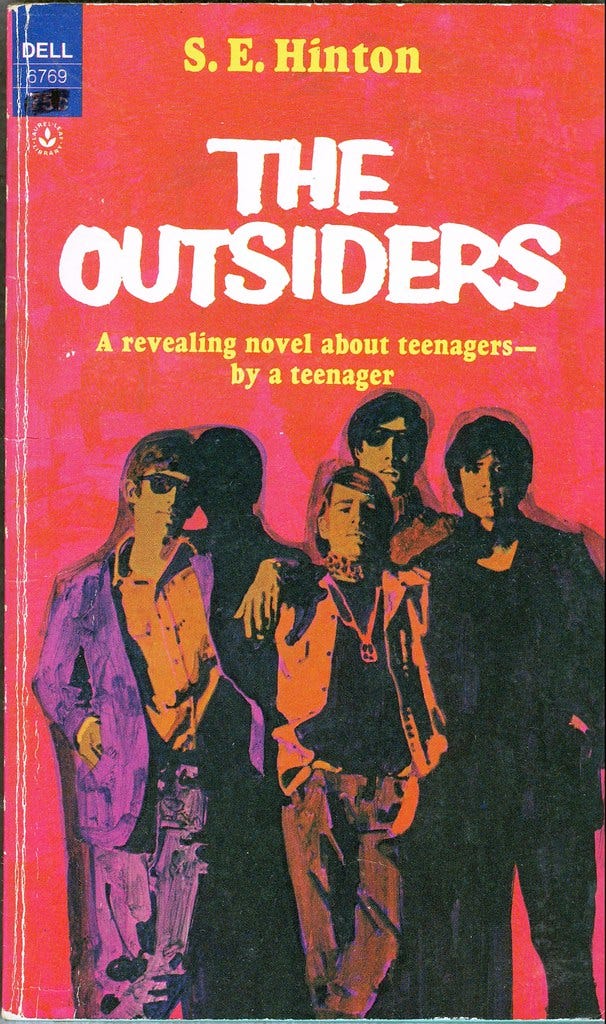 Book cover for SE Hinton’s The Outsiders, featuring a group of young men against a red and pink background.