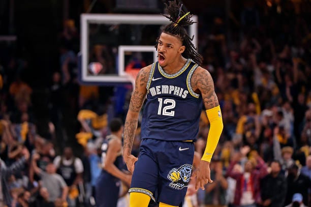 Star player for the Memphis Grizzlies Ja Morant roaring for the crowd while wearing a navy blue jersey and shorts with a yellow arm sleeve on his left arm