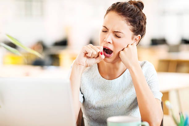 A stock image of a young woman seated, with curly brown hair tied back in a tight not. Her eyes are closed and she is in the middle of a large yawn, resting her head on one hand while the other forms a fist in front of her mouth. She is also hoping that this part of the article will be over soon.