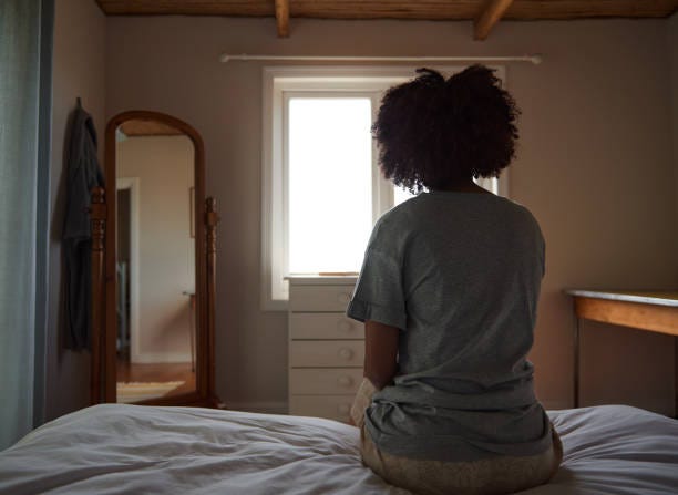 Backview of a black woman in a room looking out the window and reflecting.