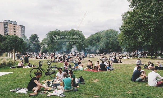 In a park, several people are sitting in groups on blankets