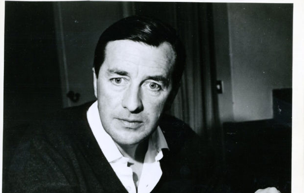 A black and white photo of Robert Bolt, a white man with dark hair wearing a white collared shirt and a black cardigan; he is looking down and to the left.