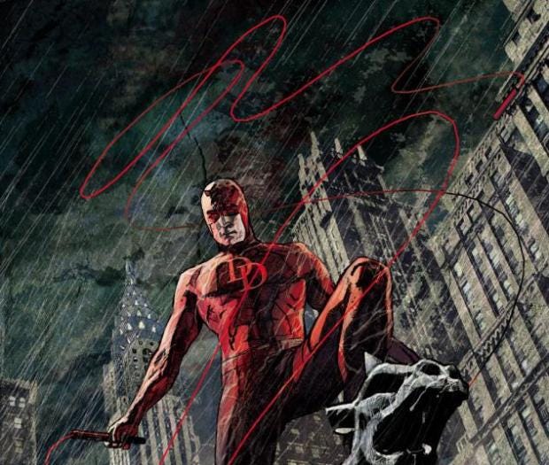 Daredevil poses on the top of a building, the rain beats down around him and his red suit stands out against the grey city background.