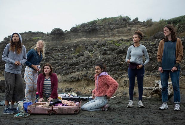 The characters huddle around a suitcase of clothing that they all share, looking exhausted on the beach.