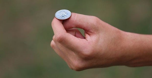 A closeup of a green background with a hand posed with a quarter on top, about to flip it.
