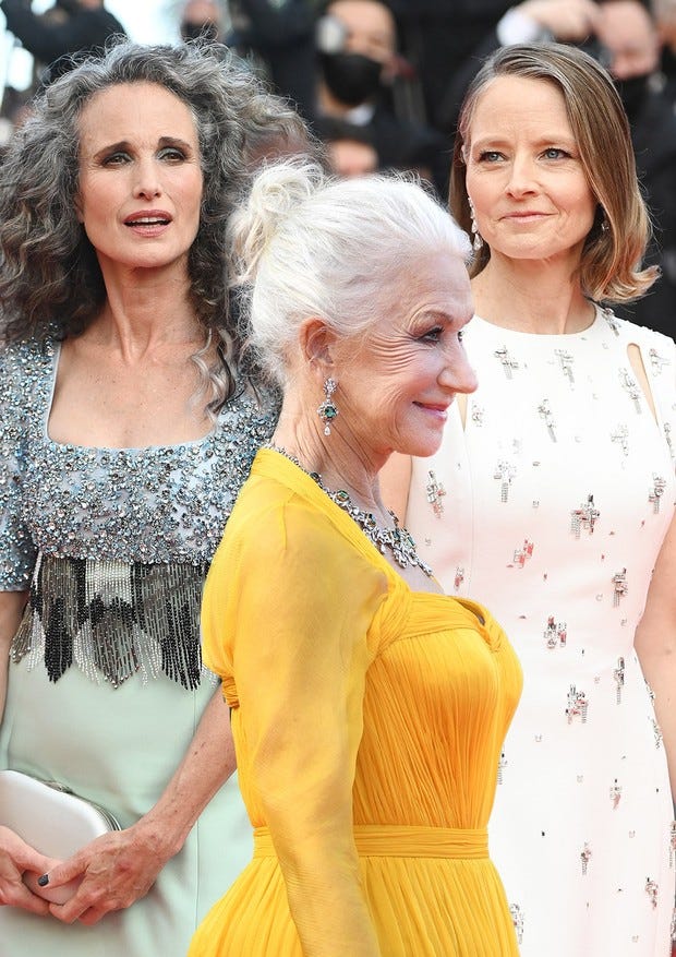 Fotografia do  Festival de Cannes, em primeiro plano a atriz Helen Mirren(76 anos) de perfil, usando um vestido amarelo e cabelo preso, totalmente branco. No fundo, as atrizes Andie MacDowell(63 anos), com cabelos soltos grisalhos e cacheados, usando um vestido prata. Ao seu lado a atriz Jodie Foster(58 anos), usando um vestido branco, cabelos soltos, loiros e com alguns fios brancos com menos destaque.