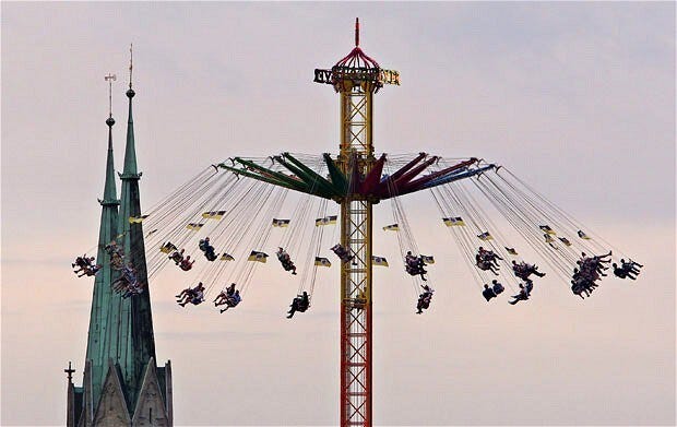 Festival-goers ride chair swings in front of the tower of the Paulskirche church | CREDIT: EPA/KARL-JOSEF HILDENBRAND
