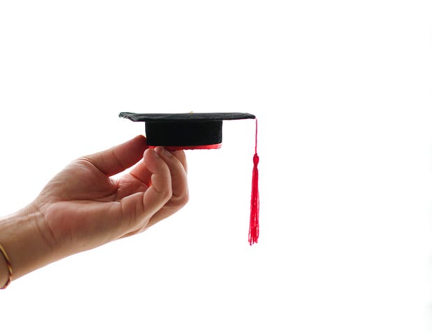 A picture of a hand holding a small mortar board as if weighing its importance.