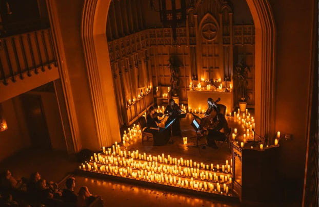 A photograph of a string quartet performing in a church with candles surrounding them in front of an audience.