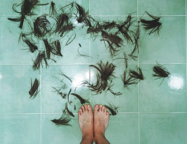 Bare feet standing on a pale green floor with cut hair strewn around it.