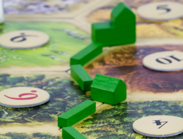 A closeup of green board game pieces placed on a board with different resource spaces