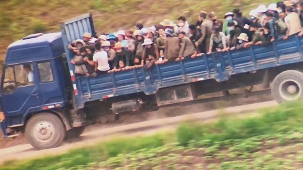 Dozens of North Koreans packed tightly on the back of a large blue truck