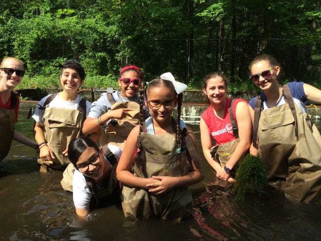 Seven girls in waders and water up to their waists smiling