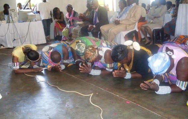 (AUTHOR NAME) and women of the Vhavenda community bowing to show respect as members of the community sit behind them.