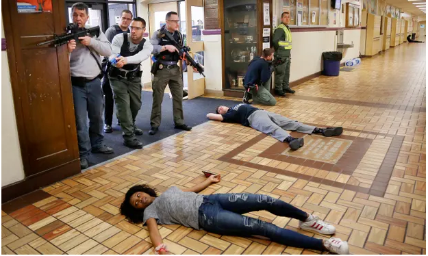 Active shooter drill at a school where men with guns role play clearing an area while students lie on the floor, pretending to be dead or injured.