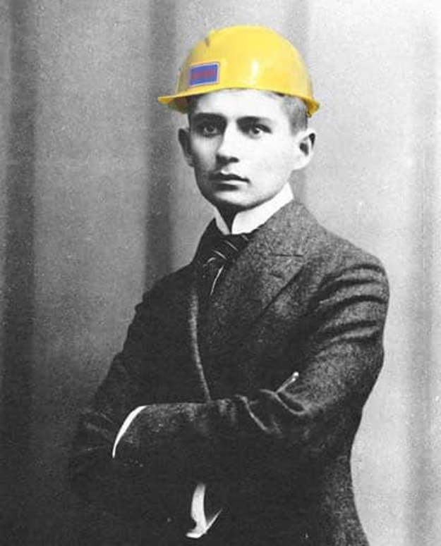 Mock-up of a young Franz Kafka photographed in b/w, looking soulful in a suit and tie, with a bright yellow hard hat superimposed on his head