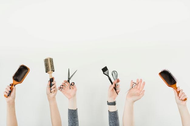 A row of hands holding up hairstyling implements (brushes, scissors, etc)