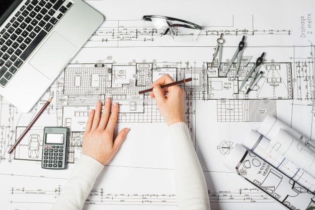 Architect’s hands drafting a floor plan over a a large sheet of paper on a desk.