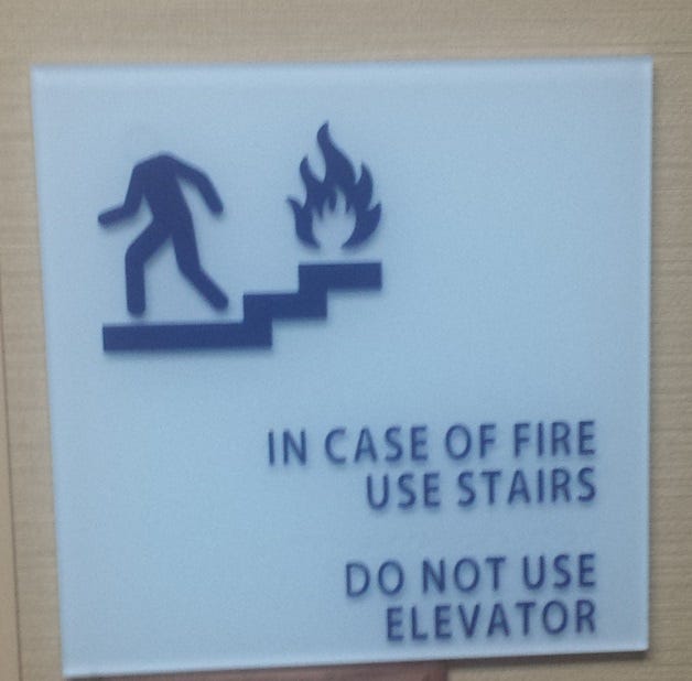 Sign instructing in case of fire use stairs using a picture of a headless stick figure.
