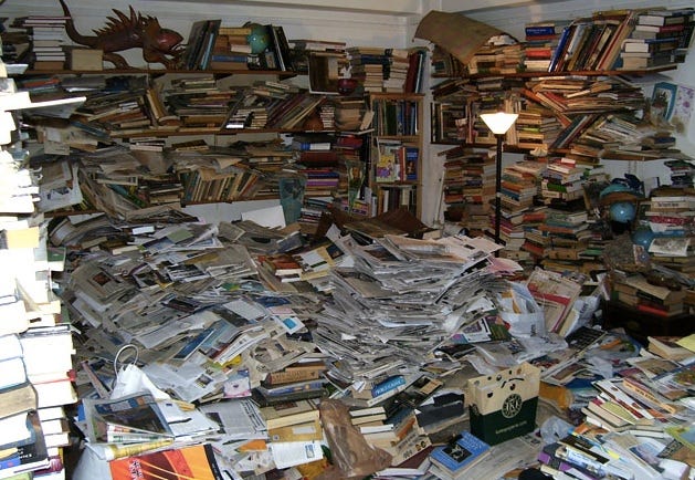 Quarto com paredes e piso repleto de livros e papéis totalmente desorganizados