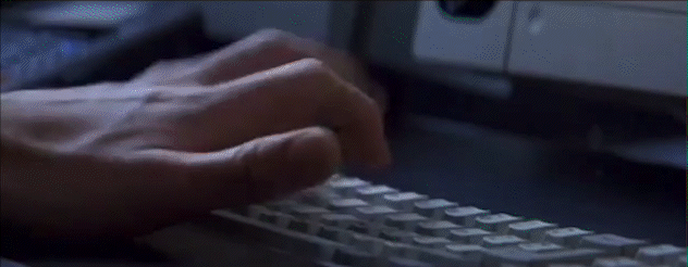 A scientist works furiously at a computer as he types with one hand as he twirls a pen with the other hand.