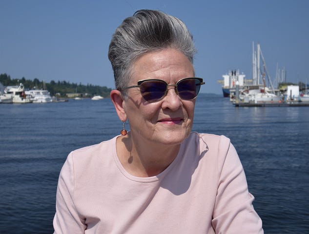 A woman in a pink shirt with water and boats behind her