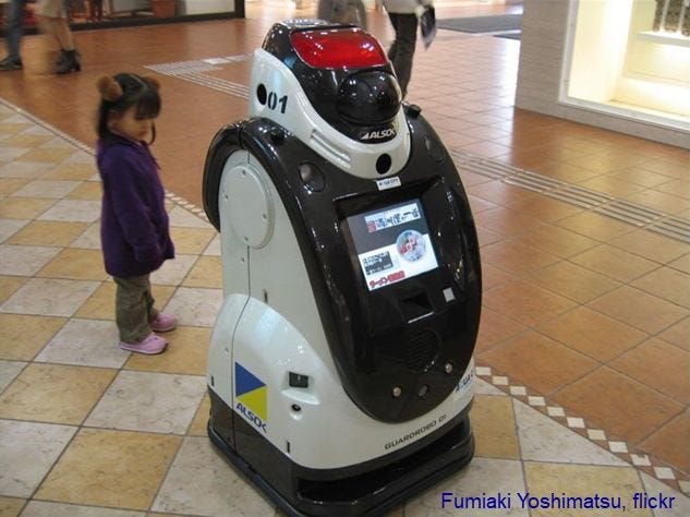 A small girl looks at a mall security robot.