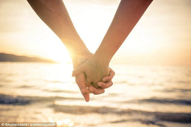 Two people hold hands in the beach on sunset with yellowish background color