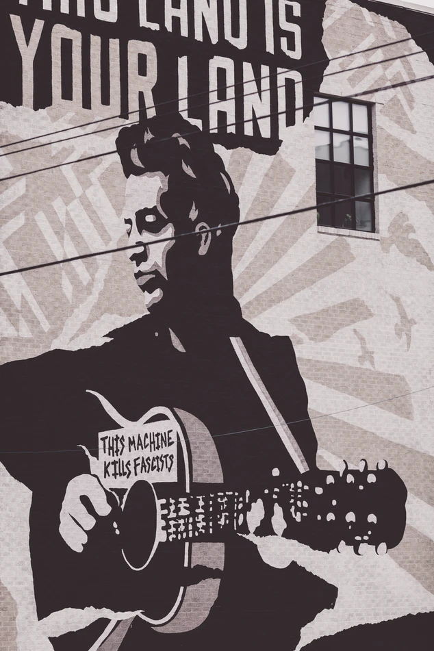 Mural of Woody Guthrie holding a guitar that says, “This machine kills fascists.”