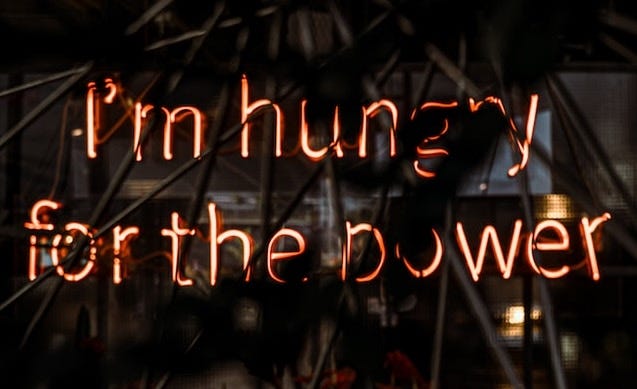 The words “I’m hungry for the power” in orange neon lights
