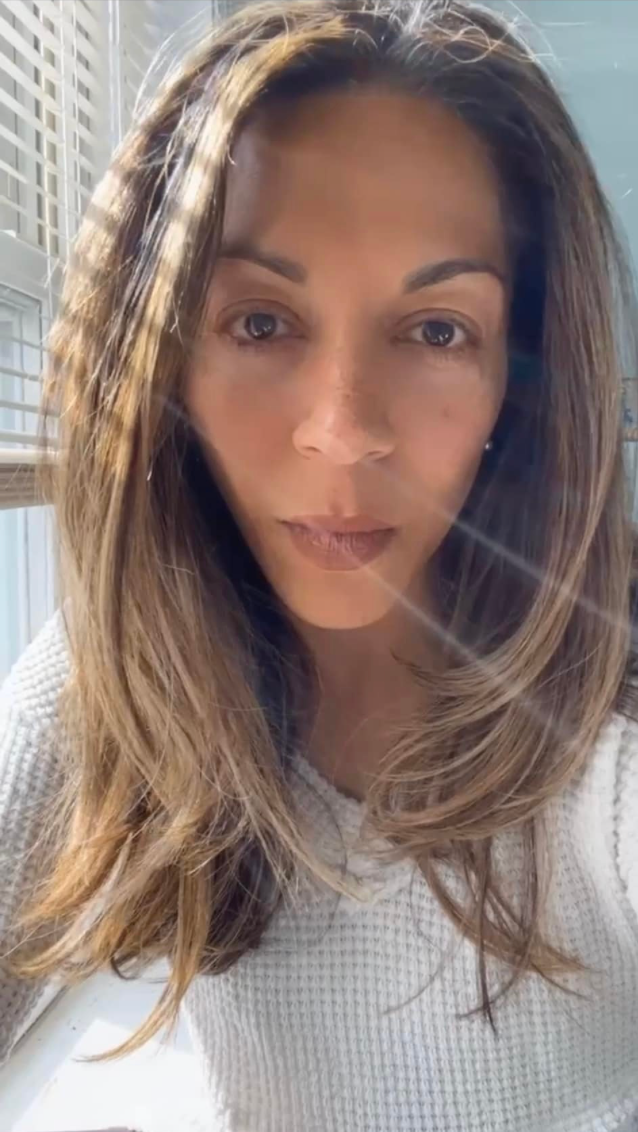 Woman of color looking at the camera in a white sweater near a window.