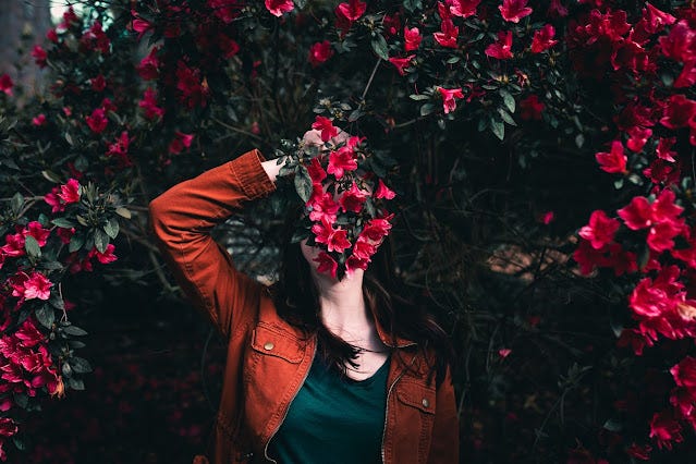 A woman hold flowers in front of her to hide her face.