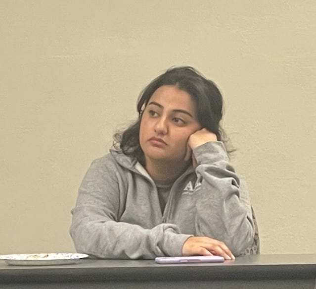 Close up of a student resting their head on their hand while listening to a presentation in a classroom.