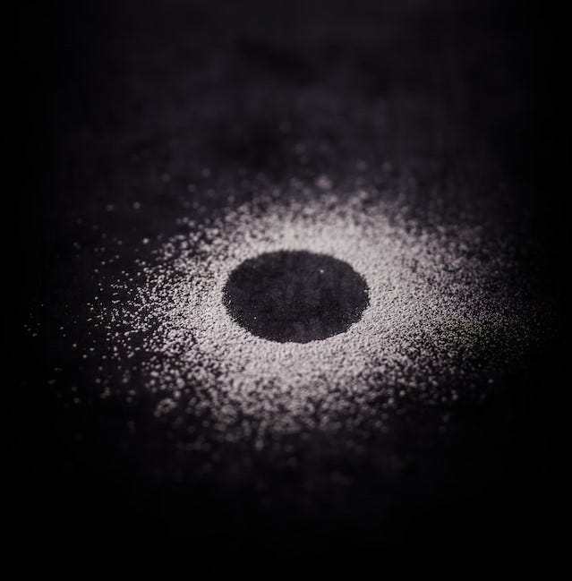 A black disk with white particles scattering away from its perimeter into a black background.