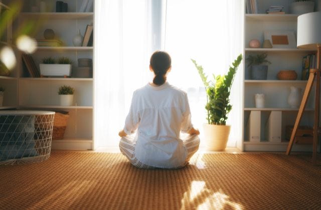 person facing a window seated on the floor while meditating