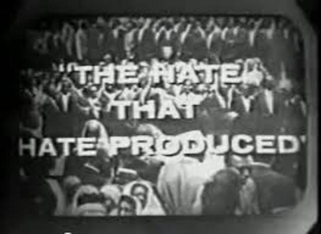 Still image of the documetnary showing members of the nation of Islam with men in suits and women wearing white headcoverings.