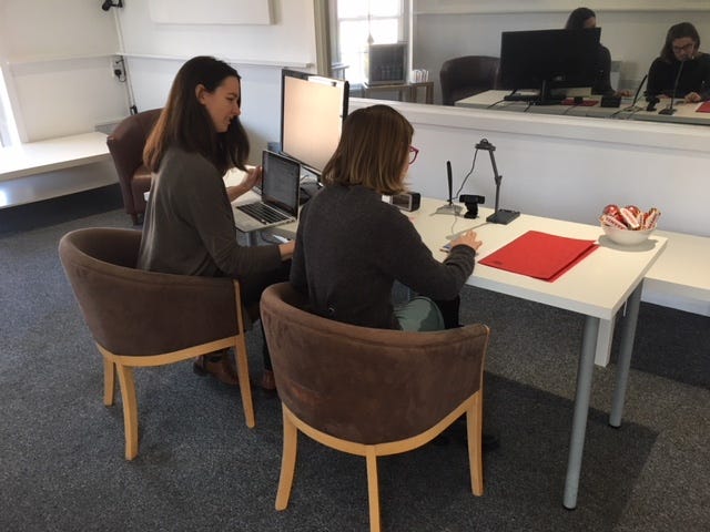 Hazel watches another woman using a mobile device in a usability testing lab