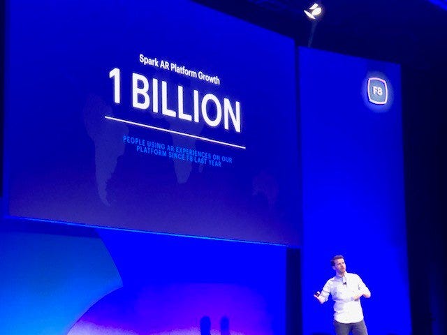 Spark AR Design Manager stands on stage, pointing to a giant blue screen with the words "1 Billion" in white on the screen.