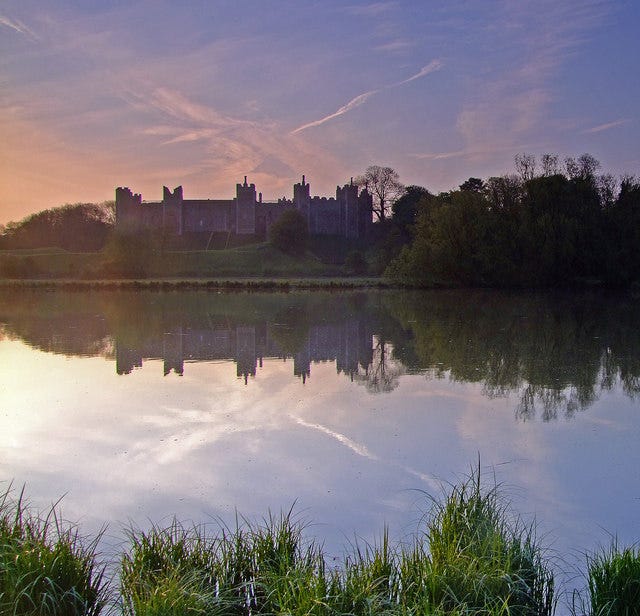 View of a crenellated castle at sunset, with a shallow lake in the foreground