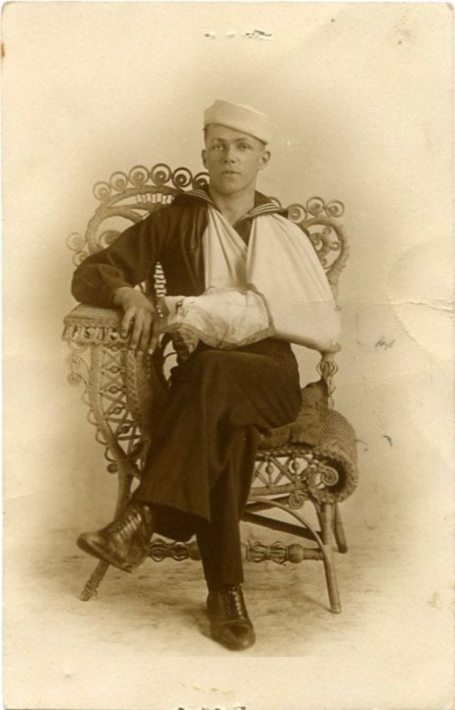 William J. Hughes from Elizabeth City, N.C., sitting on a wicker chair in his U.S. Navy uniform with his arm in a sling.