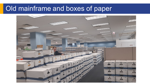 PowerPoint slide with title old mainframe and boxes of paper. Image is of Assessor Kaegi over infinite number of boxes stacked up.