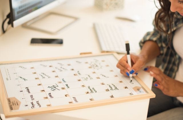 person writing on an erasable calendar board