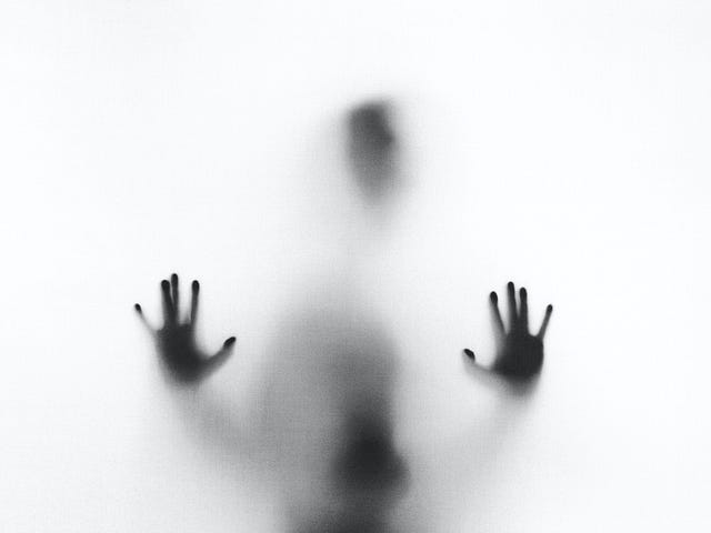A dark figure against a white background. Only the outline of the head and hands is clearly visible, the rest is blurry.