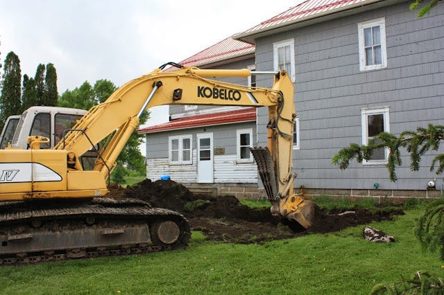Backhoe digging by farm house