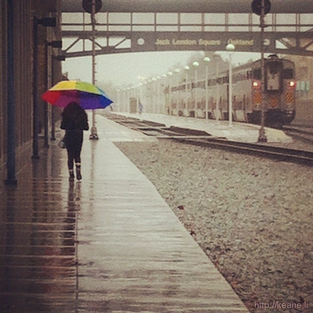 Girl with rainbow umbrella in rain at Jack London Square Amtrak in Oakland