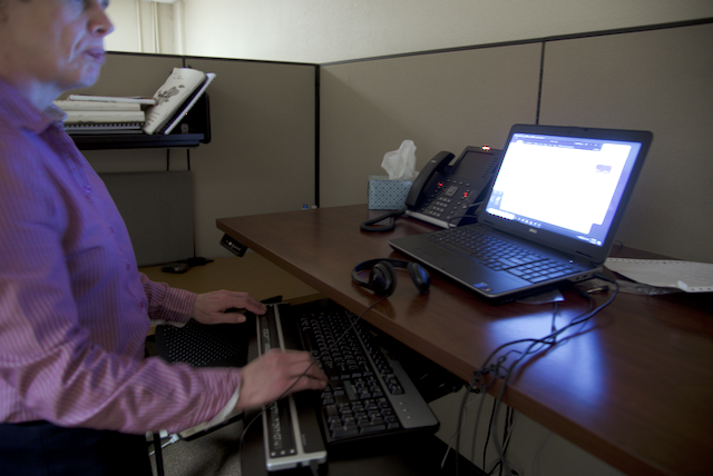 Julie stands at her desk with her hands on the keyboard using a refreshable Braille display with her computer